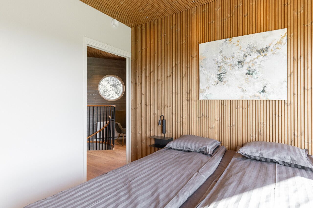 Un dormitorio con dos camas, un panel de madera con listones, un cuadro abstracto grande y un espejo redondo.