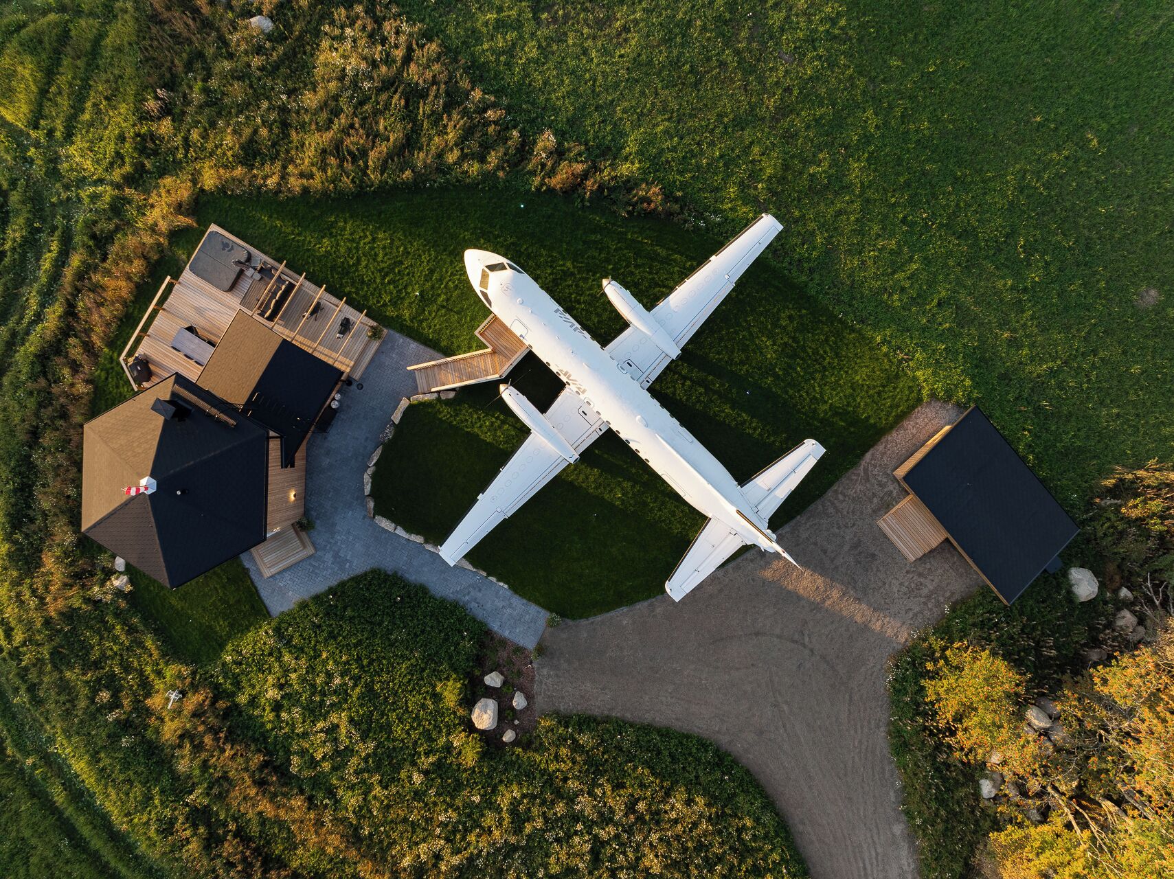 Un avion est garé sur une zone herbeuse, à proximité d’un bâtiment et d’une plateforme d’atterrissage pour hélicoptères.