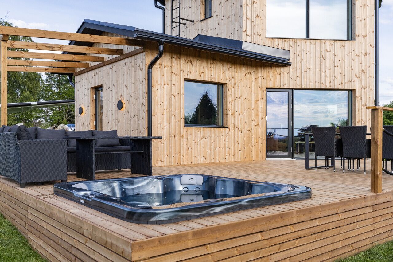 A modern wooden deck with a hot tub, outdoor furniture, and a pergola.