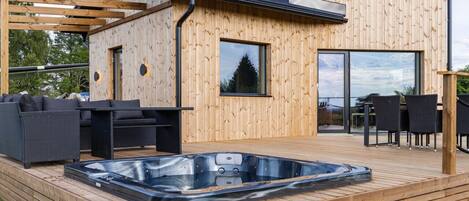 A modern wooden deck with a hot tub, outdoor furniture, and a pergola.