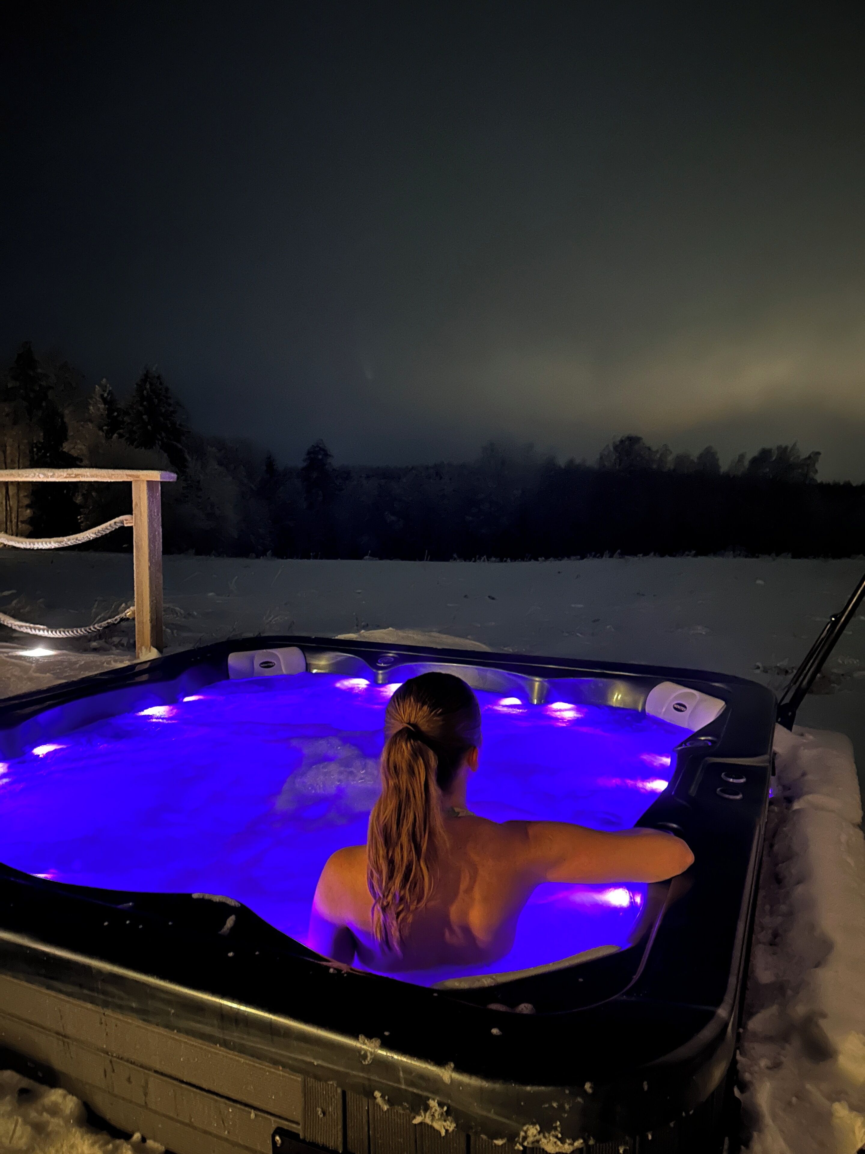 Une personne se trouve dans un bain à remous en plein air, la nuit, avec un paysage enneigé en arrière-plan.