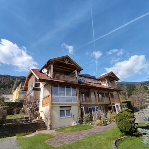 A multi-story building with balconies, a garden, and a mountainous backdrop.