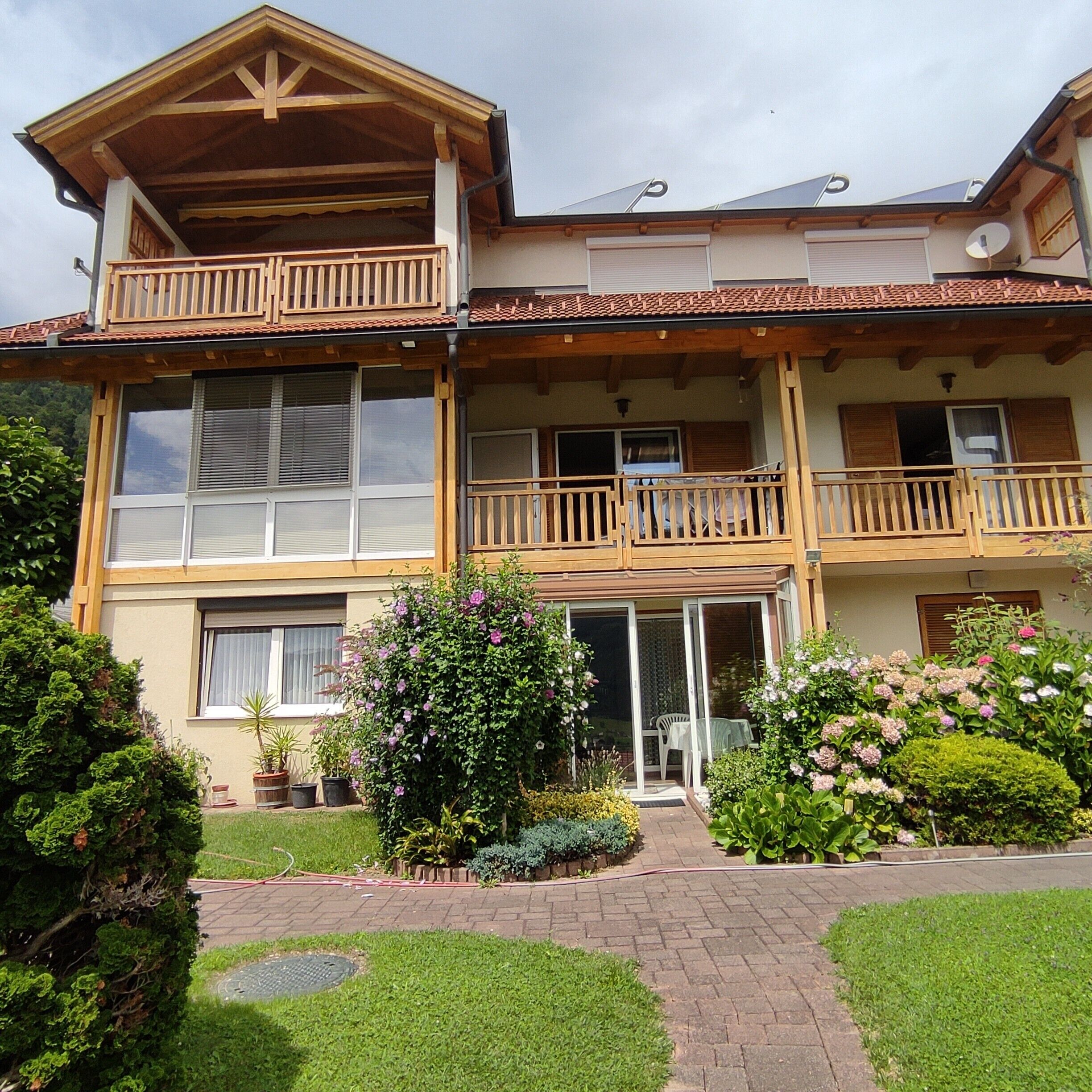 A two-story building with balconies, a garden, and a paved entrance.