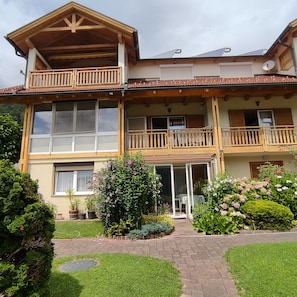 A two-story building with balconies, a garden, and a paved entrance.