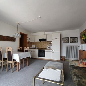 A compact kitchen with white cabinets, a dining table with chairs, a small sofa, and a radiator.