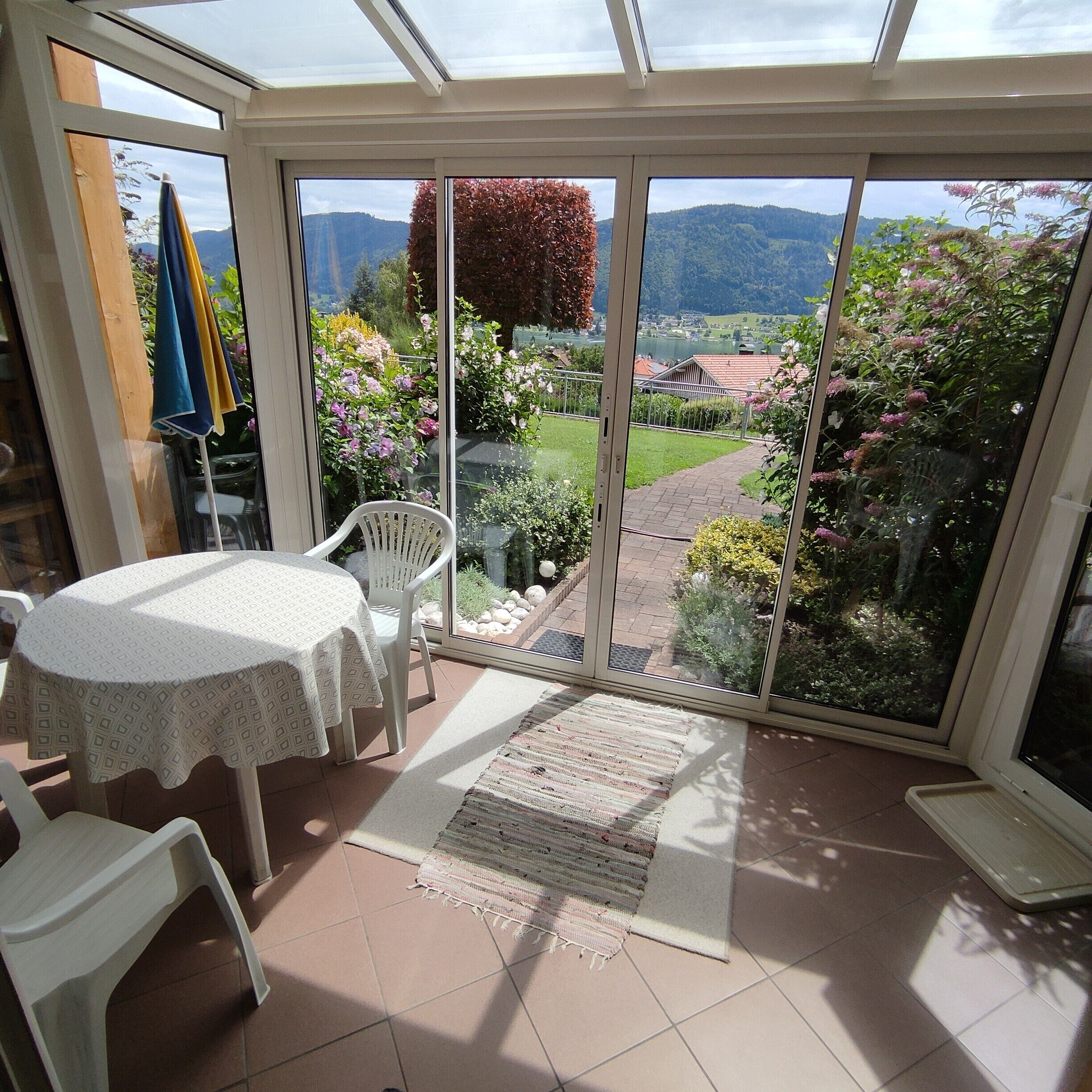 Una veranda con tavolo e sedie, vista su un giardino e un paesaggio lontano.