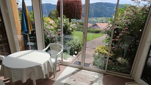 A conservatory with a table and chairs, a view of a garden, and a distant landscape.