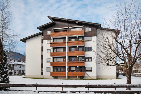 A multi-story building with balconies, a flat roof, and a snow-covered ground.