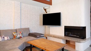A living room with a sofa, a flat-screen TV, a fireplace, and a wooden coffee table. - Holiday Apartment 'Nini's Berge' with Panoramic View, Shared Garden and Wi-Fi (Sonthofen)