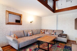 Ein Wohnzimmer mit einer Couch, einem Holztisch, einem gemusterten Teppich und einem Wandspiegel.