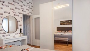 A modern bedroom with a bed, a mirror, a dresser, and a cityscape painting. - Holiday Apartment 'Nini's Berge' with Panoramic View, Shared Garden and Wi-Fi (Sonthofen)