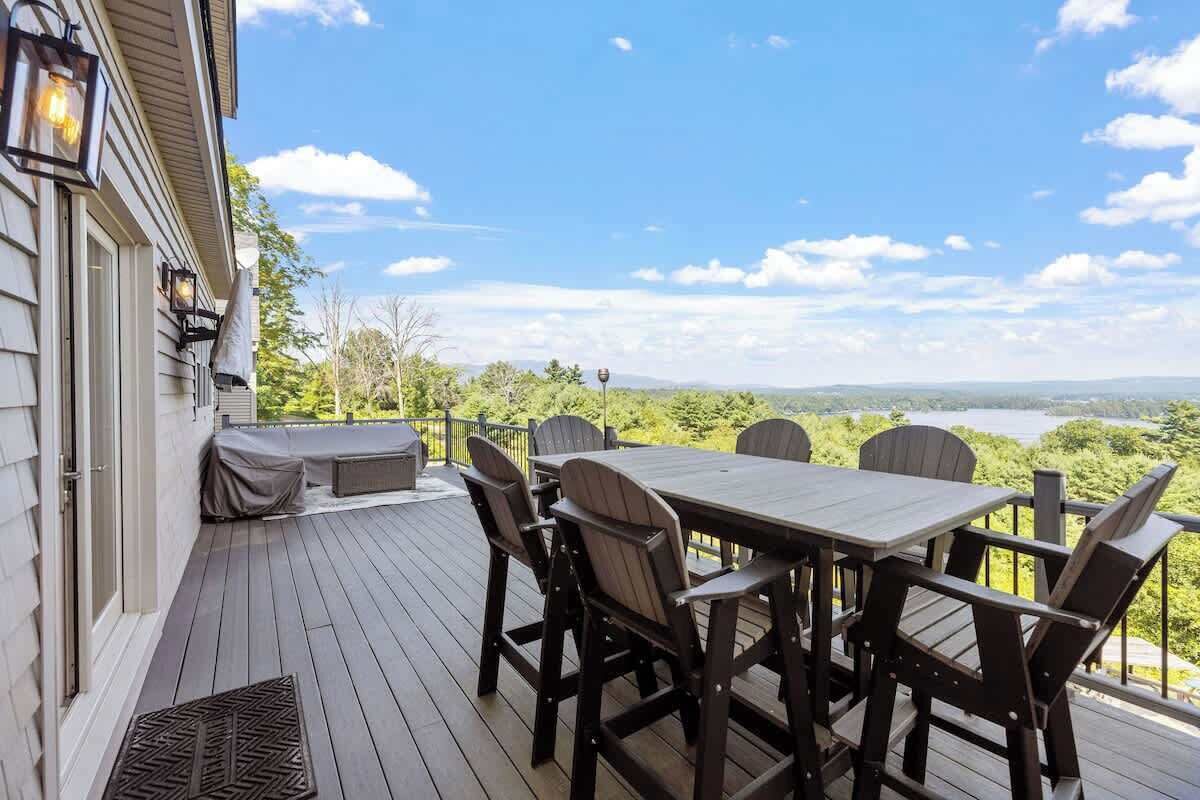 Eine Terrasse mit Tisch und Stühlen mit Blick auf einen See und viel Grün.