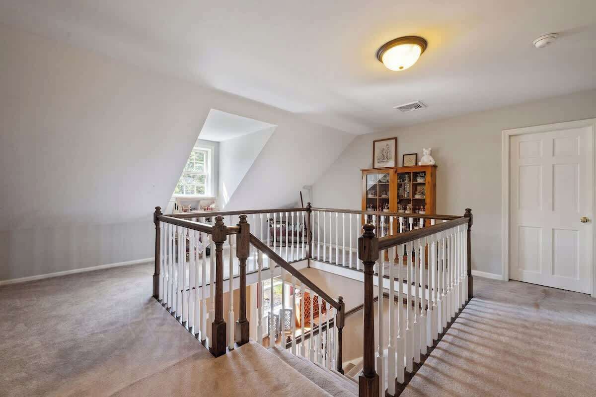 Un loft spacieux avec un plafond haut, un escalier en bois doté de rampes blanches et une grande fenêtre laissant entrer la lumière naturelle.