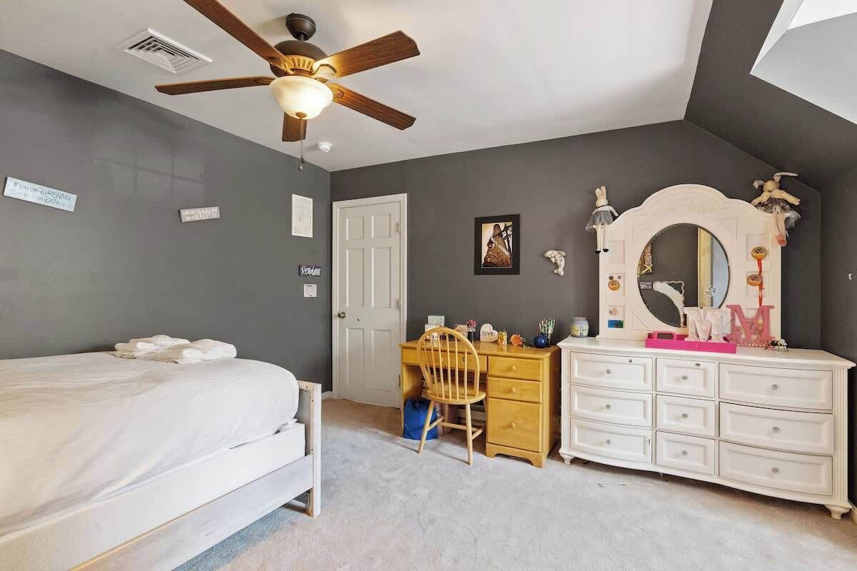 Een slaapkamer met een bed, een bureau, een dressoir, een plafondventilator en een deur.