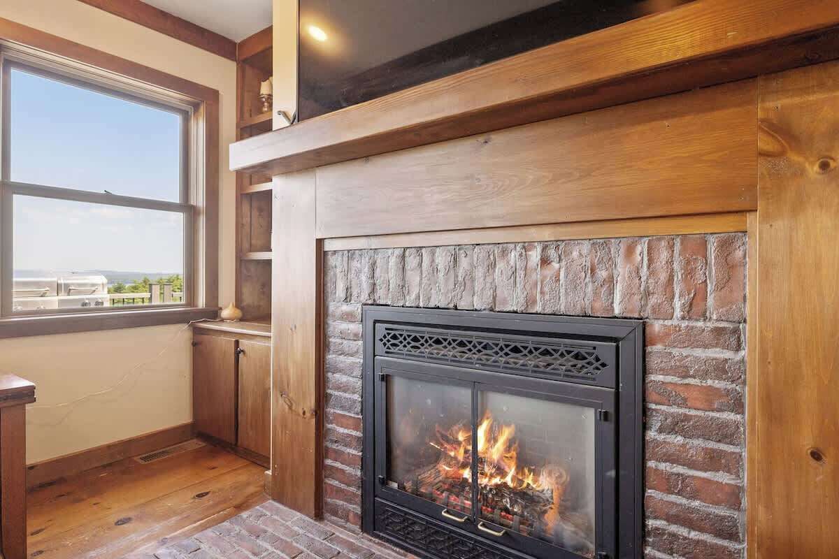 A fireplace with a brick surround, wooden beams, and a window with a view.