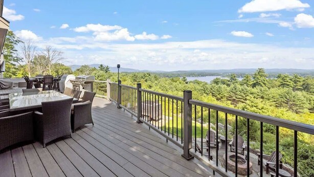 A deck with outdoor furniture, a grill, and a scenic view of a lake and forest.