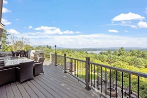 Una terraza con mobiliario exterior, una parrilla y una vista panorámica de un lago y un bosque.