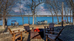 Un espacio de descanso junto al lago con un brasero y sillas Adirondack.