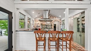 Cocina con salpicadero de ladrillo, muebles blancos y una isla grande con taburetes de bar.