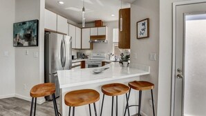 A modern kitchen with a central island, stainless steel appliances, wooden bar stools, and pendant lighting. - @ Marbella Lane - Modern 3BR Home w/ Ocean Views (Pacifica)