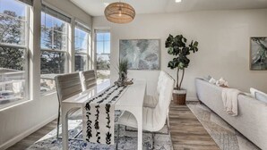 A modern dining area with a white table, chairs, and a hanging light fixture. - @ Marbella Lane - Modern 3BR Home w/ Ocean Views (Pacifica)