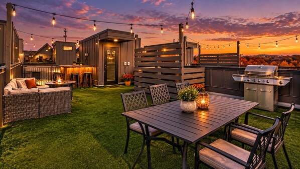 An outdoor patio with a dining table, chairs, a grill, and string lights.