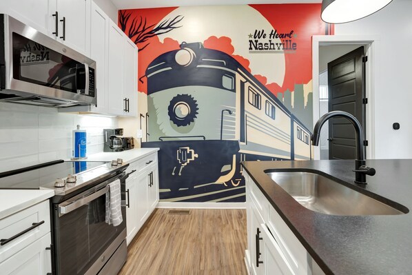 A kitchen with white cabinets, a stainless steel sink, and a mural of a train on the wall.