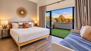 Un dormitorio con una cama grande, una cama más pequeña, un ventanal con vistas a un jardín y una lámpara fijada en la pared.
