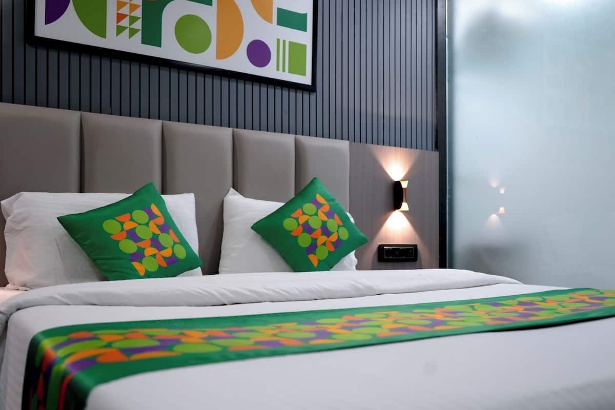 Camera d'albergo con un letto, due cuscini decorati con un motivo geometrico colorato, una lampada a parete e un'opera d'arte astratta incorniciata sopra il letto.
