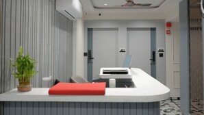 Un mostrador de recepción moderno con un portátil, un cojín rojo y una planta en maceta.
