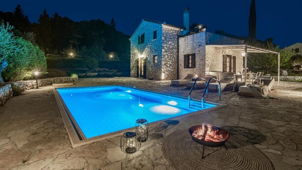 Una piscina con solárium de piedra, una fogata y asientos exteriores.