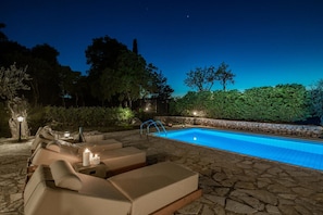 A poolside area with lounge chairs and a stone-tiled deck. - Villa Boscheto Pente (Zakynthos)