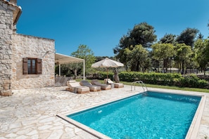 A stone building with a pool area, including lounge chairs and umbrellas. - Villa Boscheto Pente (Zakynthos)