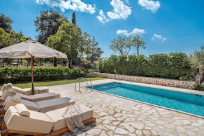 A swimming pool with lounge chairs and an umbrella, surrounded by stone tiles and greenery. - Villa Boscheto Pente (Zakynthos)