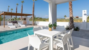 A modern outdoor pool area with a pergola, white furniture, and palm trees. - Salty Sun 4 in Kremasti (Rhodes)