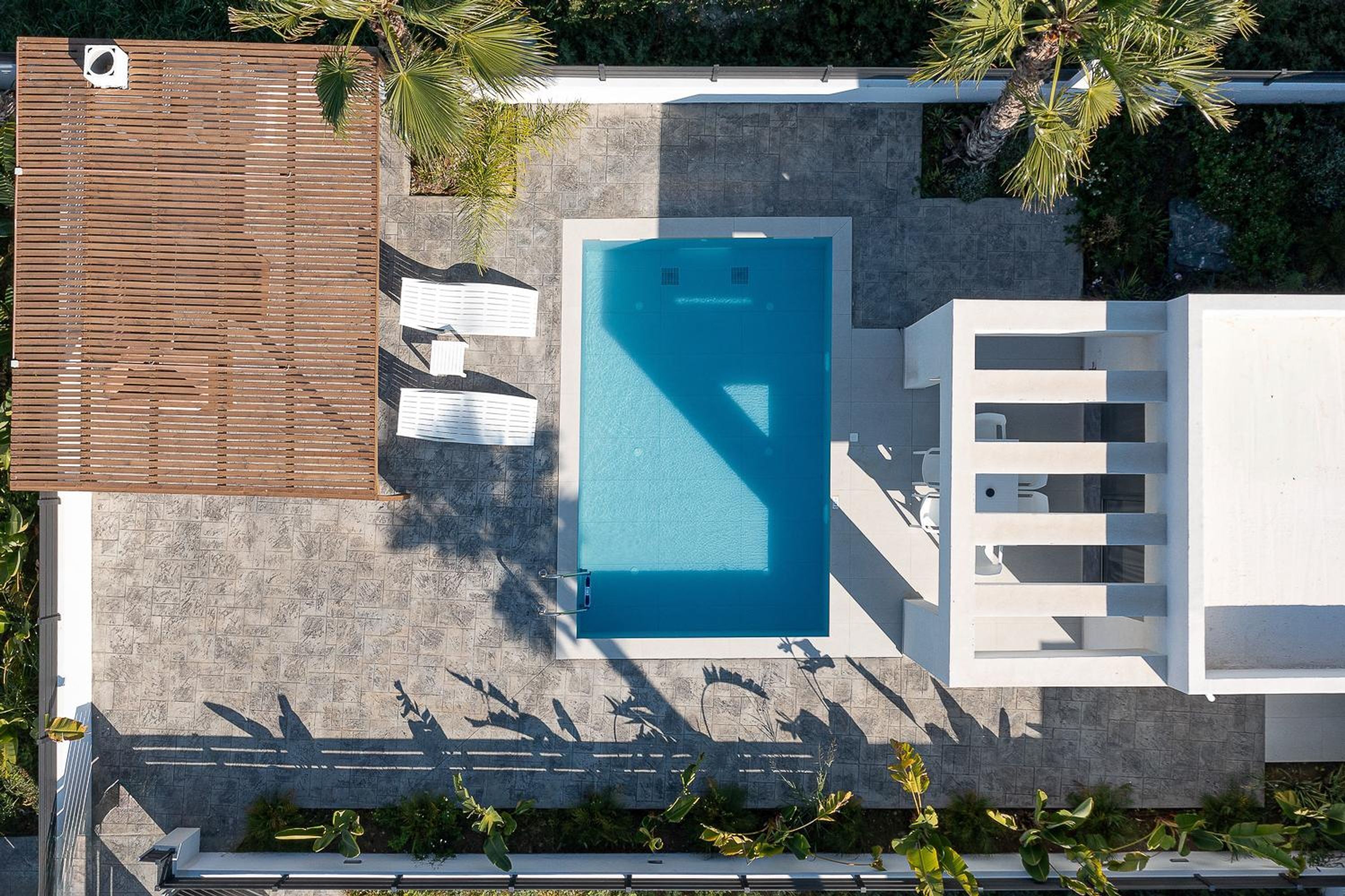 An aerial view of a modern pool area with a rectangular pool, white lounge chairs, and a wooden deck.