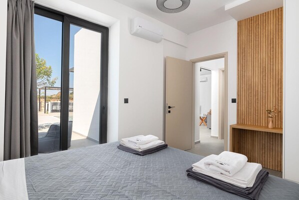 A modern hotel room with a large bed, a sliding glass door to the outside, a wooden wardrobe, and a small seating area visible through the door. - Zen Club 9 in Kolympia (Rhodes)