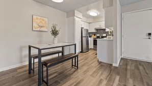 A modern kitchen with white cabinets, stainless steel appliances, and a dining area with a bench and table. - Pool -Gym- Great for Mid/Long Stays (Mesa)
