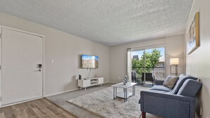 A living room with a grey sofa, a white entertainment unit, a grey rug, and a balcony with a view of the city. - Pool -Gym- Great for Mid/Long Stays (Mesa)