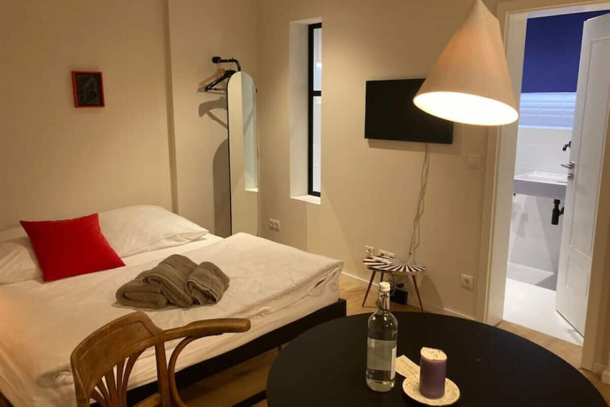 Una habitación de hotel con cama, una silla, una mesa, una botella y una lámpara.