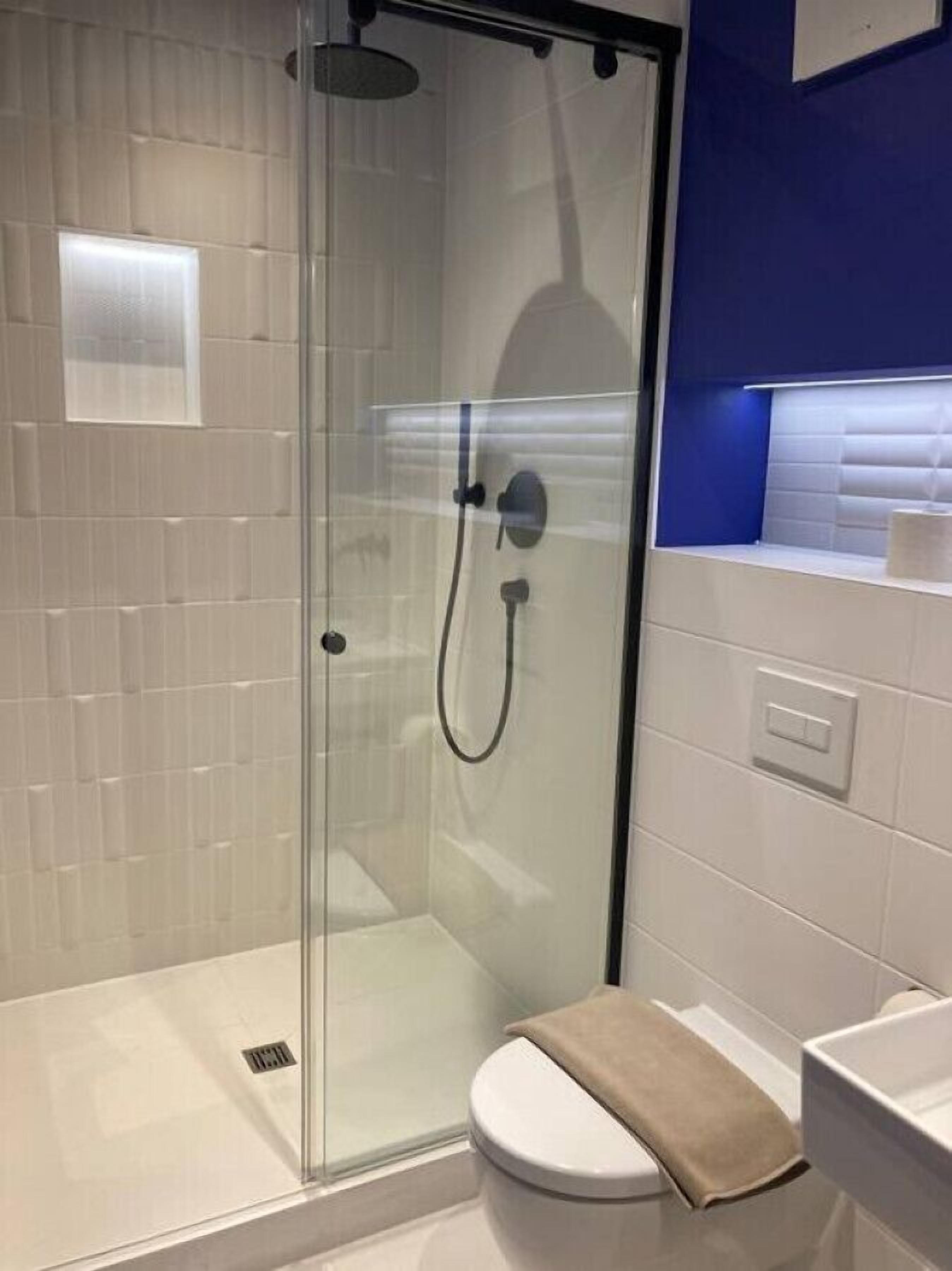 A modern bathroom with a glass-enclosed shower, white tiles, and a blue accent wall.