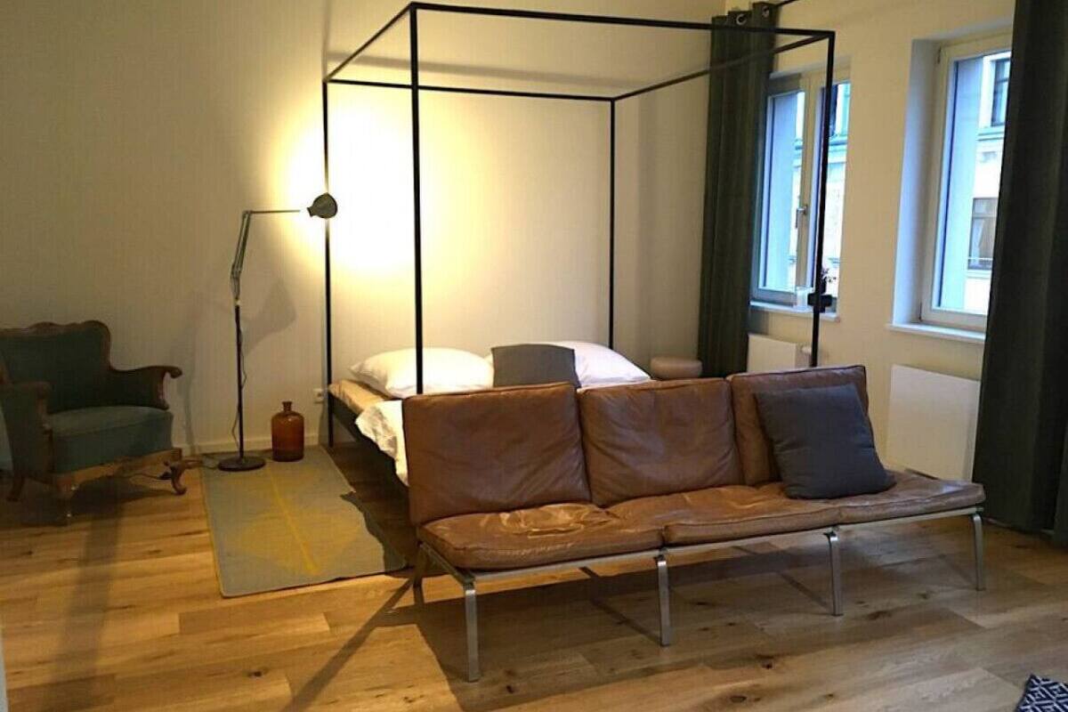 Un dormitorio con una cama con dosel, un sofá de cuero, una lámpara de pie y piso de madera.