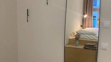 A room with a large mirror, a bed, a nightstand, and a window with curtains.