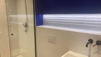 Un baño con cabina de ducha de vidrio, un lavabo blanco y una pared azul decorativa.