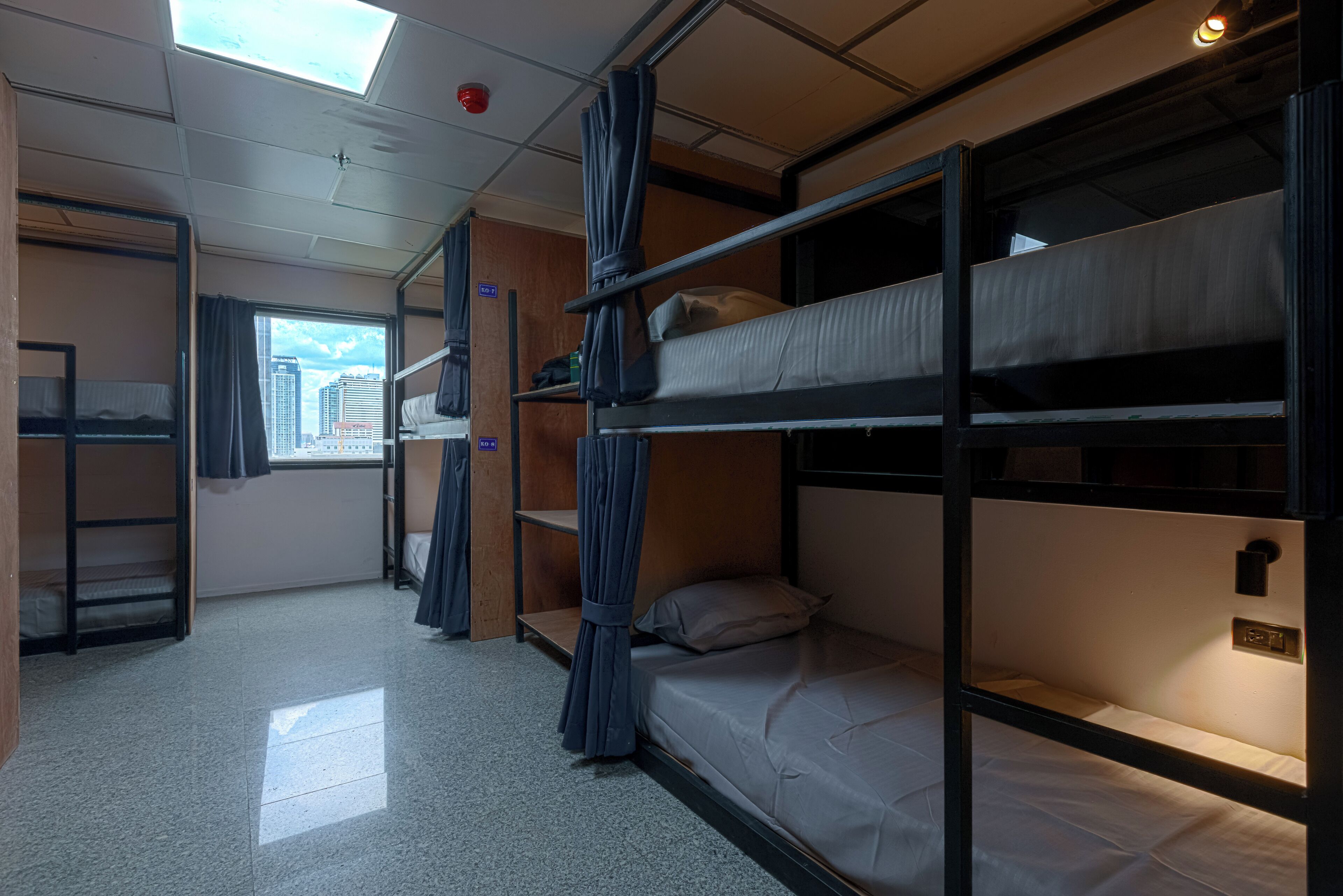 A train compartment with bunk beds, a skylight, a window with a city view, and a small shelf with personal items.
