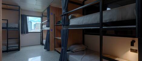 A train compartment with bunk beds, a skylight, a window with a city view, and a small shelf with personal items.