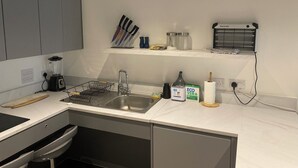 A modern kitchen with a built-in dishwasher, a sink, and a countertop with a blender and a cutting board. - Remarkable 3-bed Apartment in London (Erith)