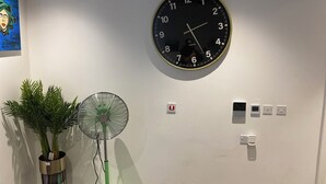 A wall-mounted clock, a standing fan, and a potted plant in a corner. - Remarkable 3-bed Apartment in London (Erith)
