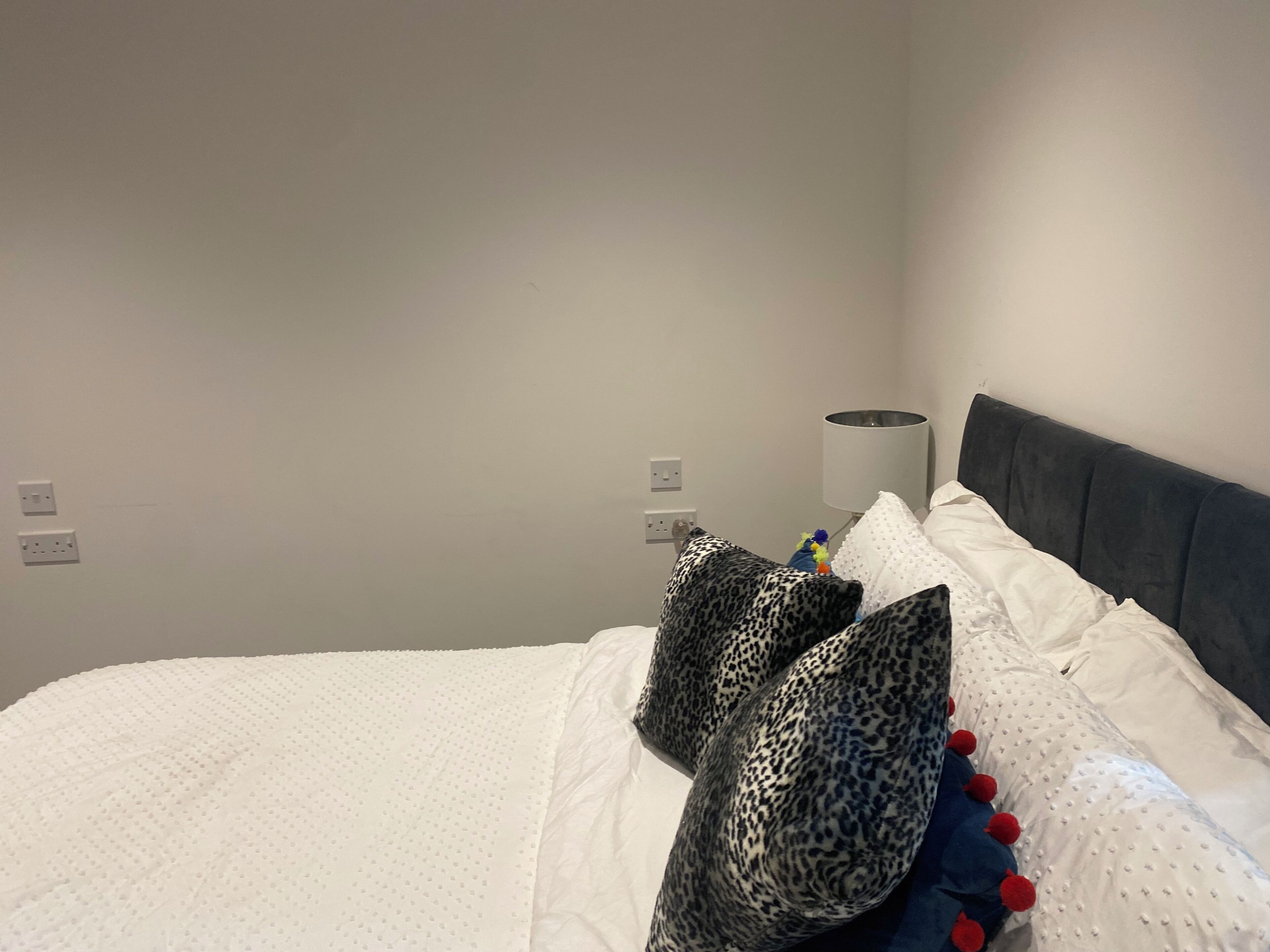 Un lit avec une literie blanche, une tête de lit grise et des coussins décoratifs.