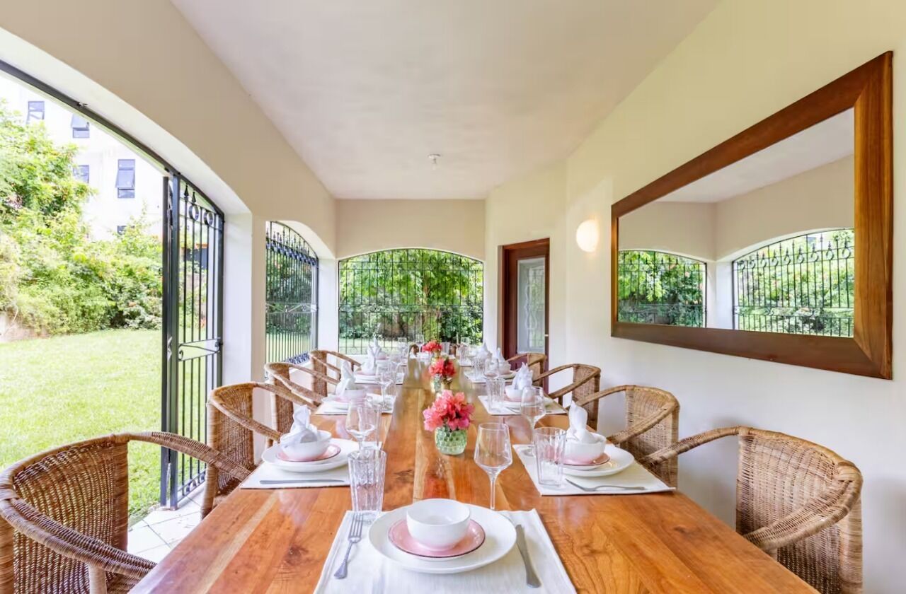 A dining area with a long wooden table set for six, surrounded by wicker chairs.